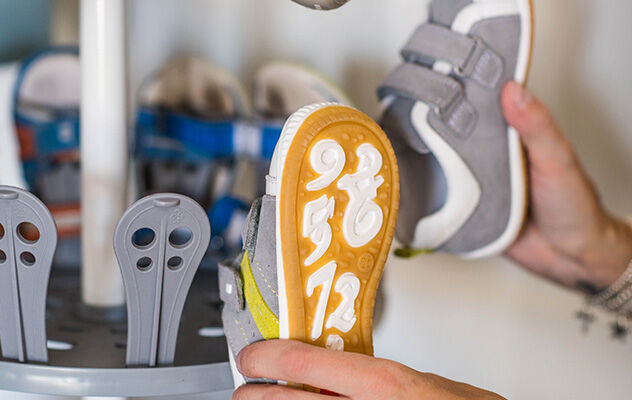 Eine junge Frau hängt Kinderschuhe an ein Schuhregal